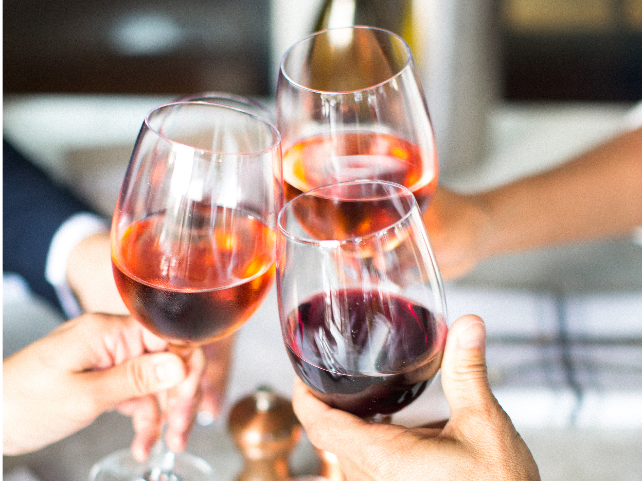 Three hands clinking glasses of rosé and red wine in a celebratory toast at True Food Kitchen.