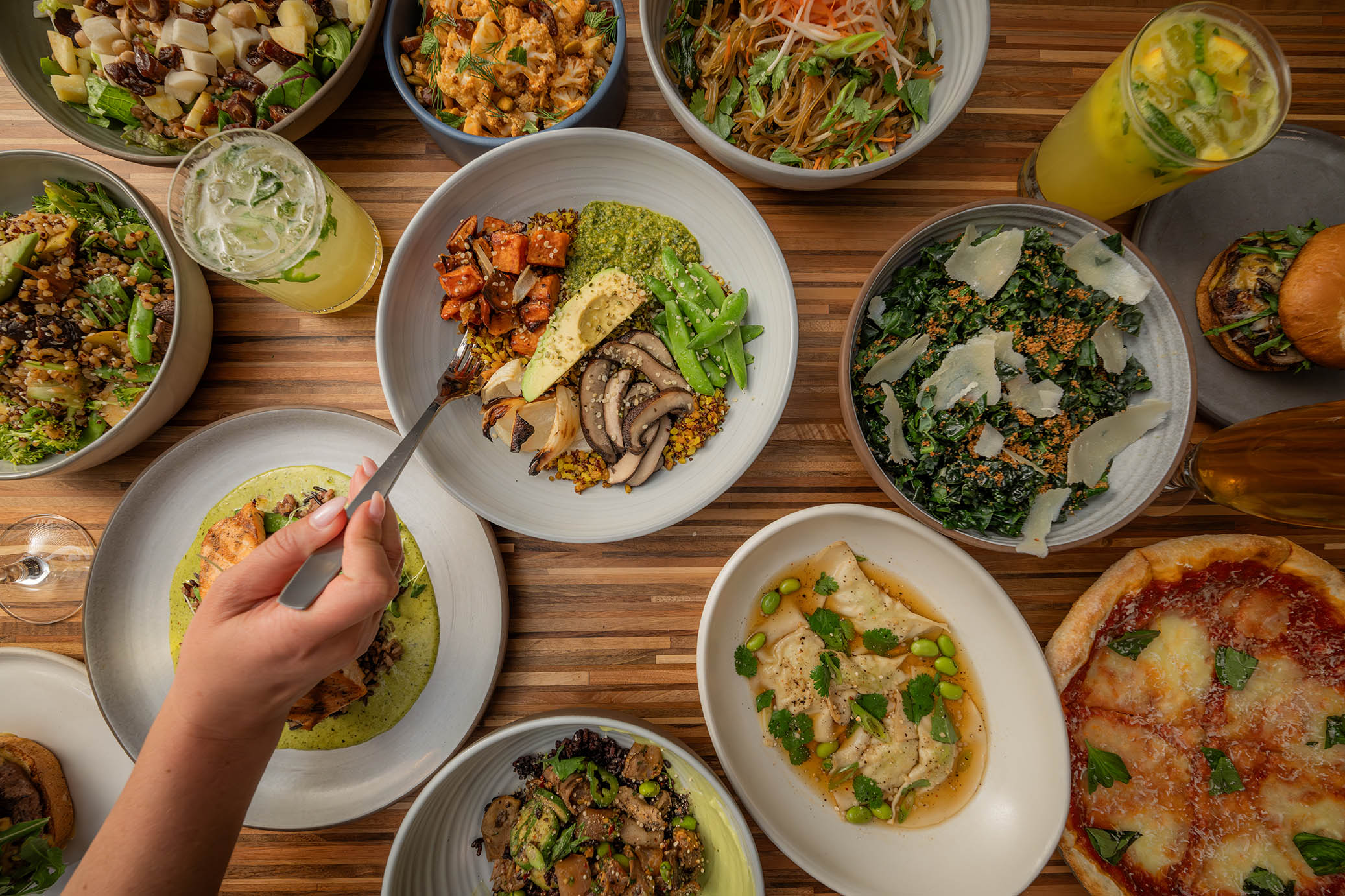 An assortment of dishes from True Food Kitchen's menu, including colorful salads, pizzas, and other fresh items, all beautifully arranged on wooden boards and plates.